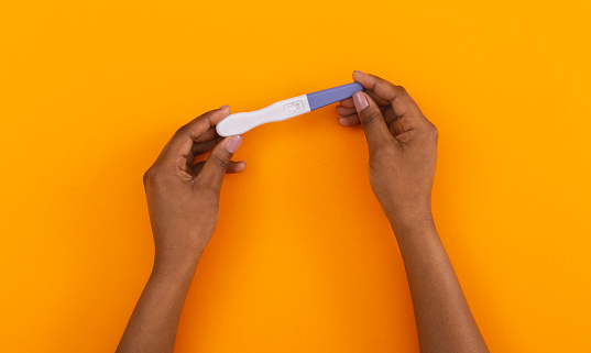 Baby planning concept. Pregnancy or ovulation test with blank result place in african american woman's hands over orange background, panorama