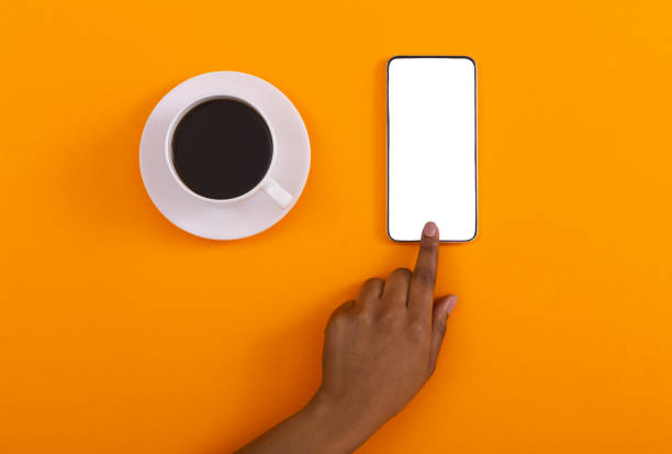 istock Hand touching blank smartphone and coffee cup on orange background 1184175883