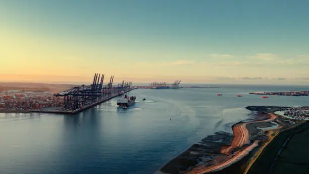 Photo of Sunrise over Felixstowe Container Port as two tugs shepherd a container ship away from the harbour wall