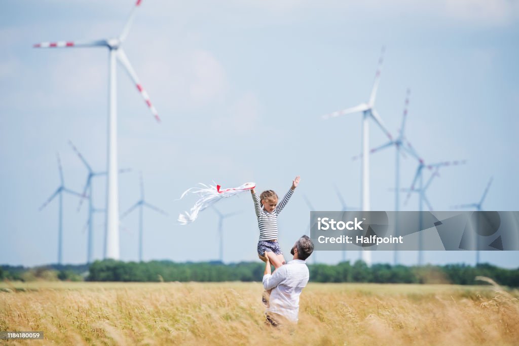 Padre maduro con una hija pequeña de pie en el campo en el parque eólico. - Foto de stock de Aerogenerador libre de derechos