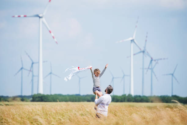 père mûr avec la petite fille restant sur le domaine sur le parc éolien. - farm scenics landscape alternative energy photos et images de collection
