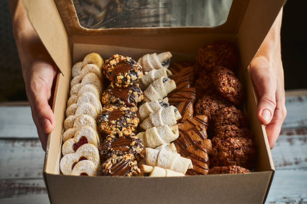 femme retenant une boîte remplie de mini gâteaux de pâtisserie de noel - cookie baked sweet food food photos et images de collection