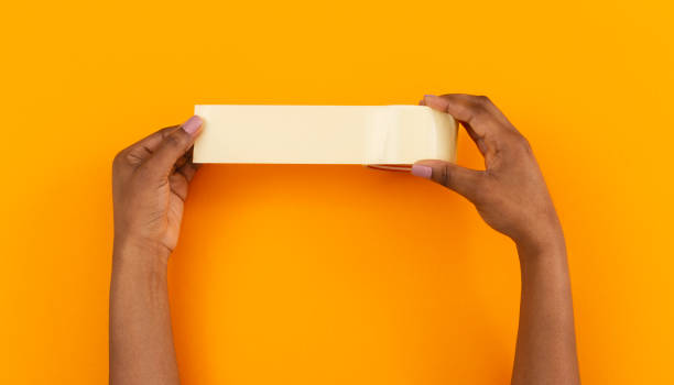 roll of duct tape in female hands over orange background - packing duck imagens e fotografias de stock