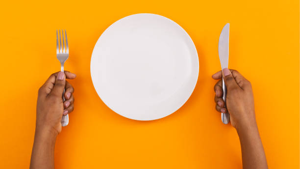 istock Empty plate and cutlery in woman's hands on orange background 1184181922