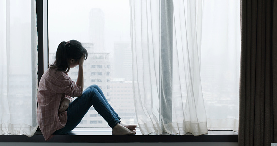 asian woman cry and sit by window on a rainy day