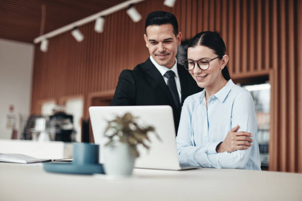 istock Smiling businesspeople standing in an office working on a laptop 1184184941