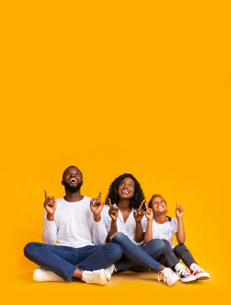 famiglia afro di tre persone seduta sul pavimento e rivolta verso l'alto - moving up child pointing looking foto e immagini stock