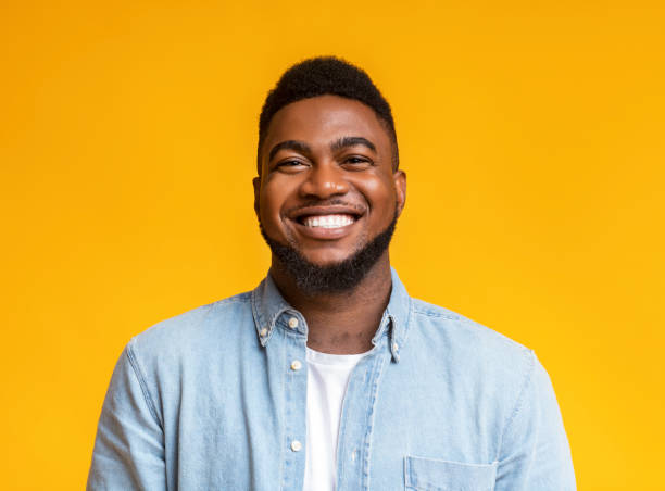 Portrait of cheerful bearded black man over yellow background Portrait of young smiling african american guy with beard over yellow background, copy space men hairstyle afro cool stock pictures, royalty-free photos & images