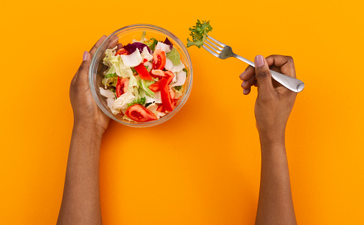 Weight Loss Concept. Black woman having fresh vegetable salad as a meal on orange studio background, top view