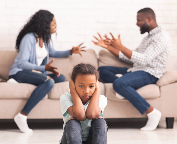 Upset black girl closing ears for not listening parents arguing Children and divorce concept. Upset african girl closing ears not to listen parents arguing, sitting on floor at home, feeling lonely. man closing ears photos stock pictures, royalty-free photos & images