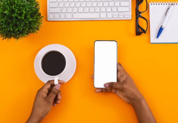istock Black woman holding blank smartphone and drinking coffee at workplace 1184188404
