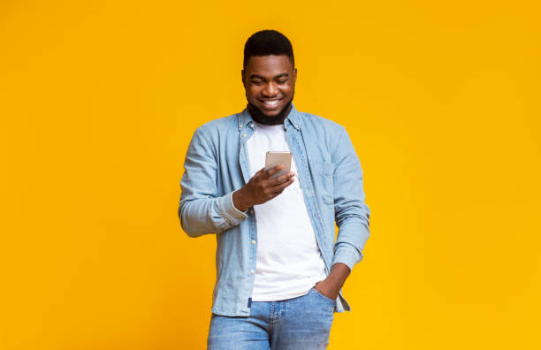 istock Cheerful black guy reading message on smartphone over yellow background 1184188686
