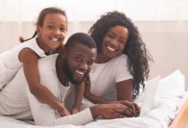 istock Black parents and their daughter lying on bed using laptop 1184190090