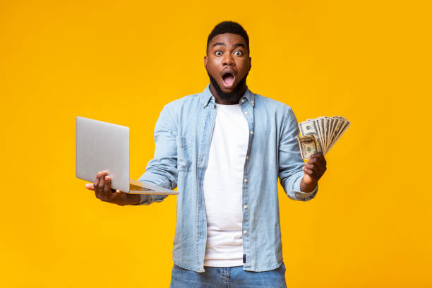 istock Dazed afro man with cash and laptop over yellow background 1184190206