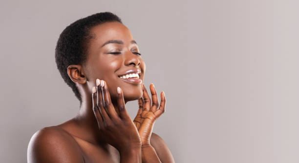 Happy afro woman touching soft smooth skin on her face Face lifting concept. Happy black woman with closed eyes touching soft smooth skin on her cheeks over grey background, panorama indulgence stock pictures, royalty-free photos & images