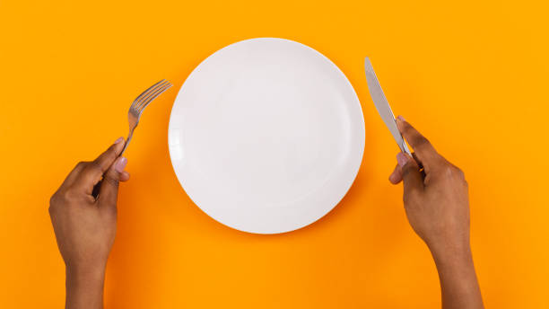 Black female hands holding empty plate on orange background, top view, free space Lunch time. Top view of empty plate with fork and knife in black woman's hands on orange background, panorama restaurant table layout stock pictures, royalty-free photos & images