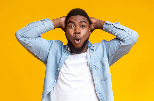 istock Amazed black guy holding hands behind head on yellow background 1184191965