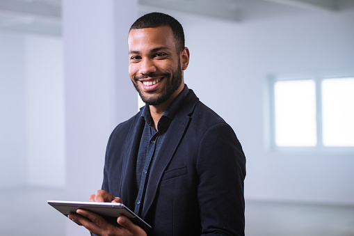 Portrait of smiling businessman using digital tablet in unfurnished office.