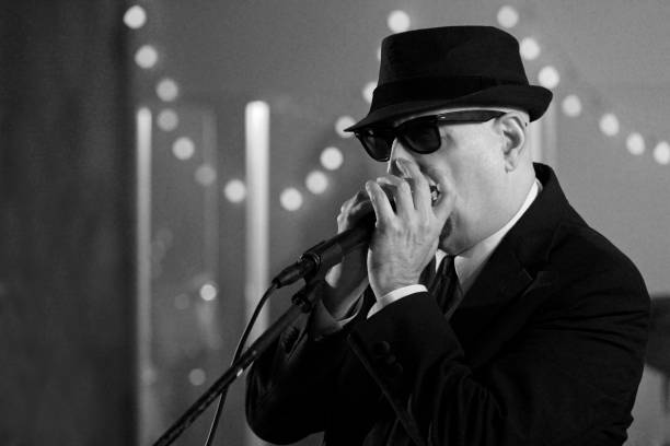 Harmonica player wearing a fedora hat and sunglasses in a live performance, black and white Blues music live on stage at a Performing Arts Event. Image shot with available light and Canon 5D Mark 4, EF 70-200mm f/2.8L lens. harmonica stock pictures, royalty-free photos & images