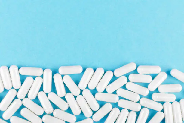 Photo of white medicine capsules on blue background with copy space