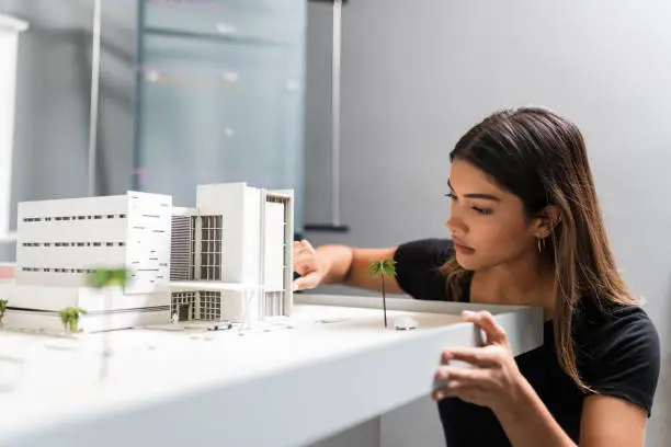 Young good looking female engineer analyzing model at desk in architect office