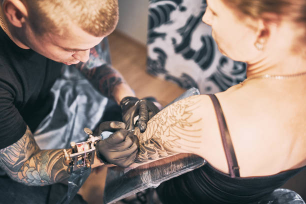tattoo-künstler machen ein tattoo auf einer schulter - tattoo men human arm shoulder stock-fotos und bilder