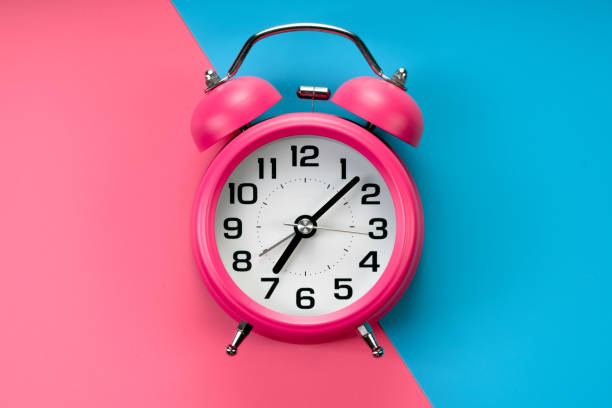 istock pink  alarm clock on pink blue background 1184213744