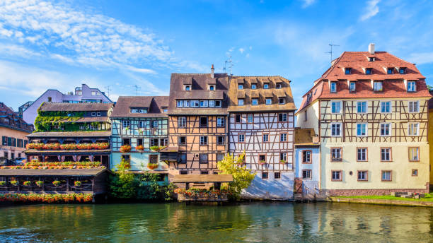 Half-timbered buildings lining the river Ill in the Petite France quarter in Strasbourg, France. Panoramic front view of typical half-timbered buildings with pastel facades lining the river Ill in the Petite France quarter in Strasbourg, France, on a sunny morning. france village blue sky stock pictures, royalty-free photos & images