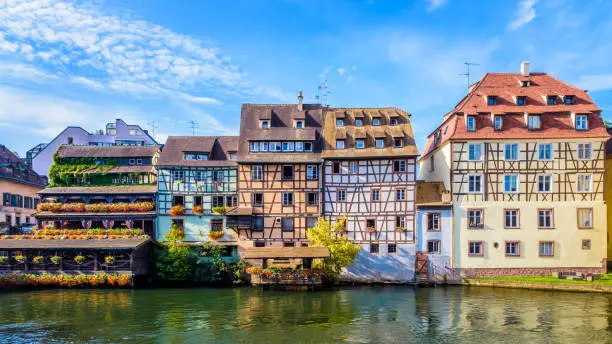 Panoramic front view of typical half-timbered buildings with pastel facades lining the river Ill in the Petite France quarter in Strasbourg, France, on a sunny morning.