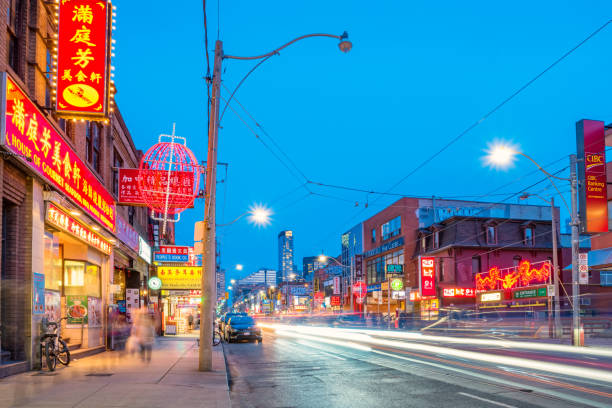 Cars and pedestrians move along Dundas Street in Chinatown, downtown Toronto, Ontario, Canada at twilight blue hour.