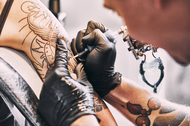 tattoo kunstenaar het maken van een tatoeage op een schouder - tatoeëren stockfoto's en -beelden