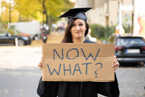 triste estudiante graduado de pie con ahora lo que placard - placard holding celebration women fotografías e imágenes de stock