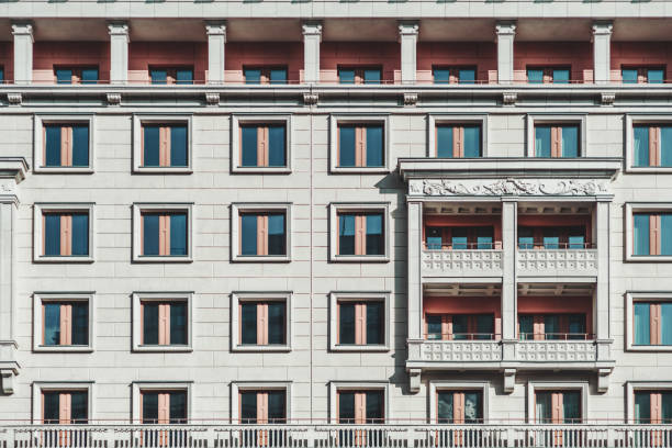 A grayish facade of a modern multi-storey building made in a typical modern Russian architecture style in Moscow: plenty of windows, balconies, bas-relief; a regular house frontage texture