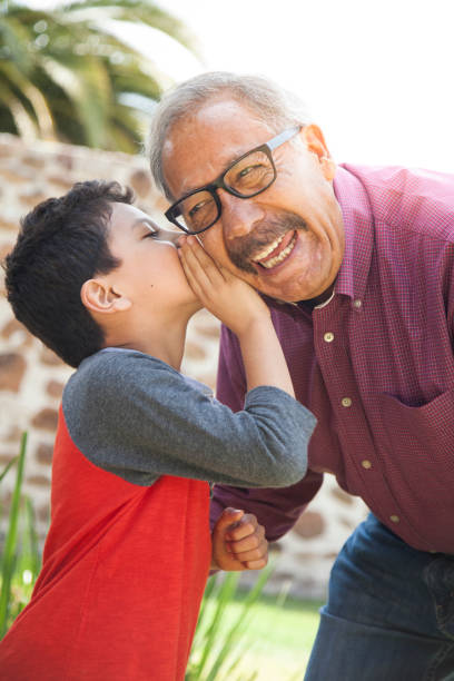 latinx niño susurra secreto al abuelo - whispering grandparent child grandfather fotografías e imágenes de stock