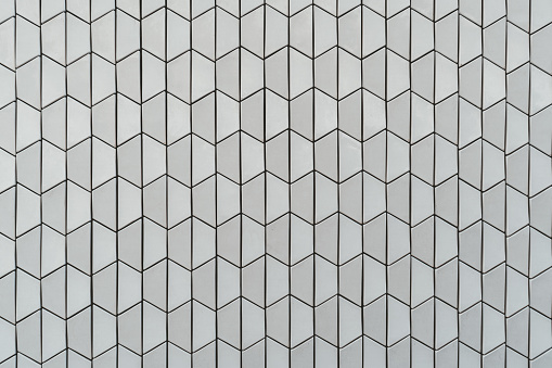 A frontal view of a modern bright ceramic or stone texture consisting of vertically placed trapezes; an evenly lit textured wall outdoors in Belem district of Lisbon, Portugal