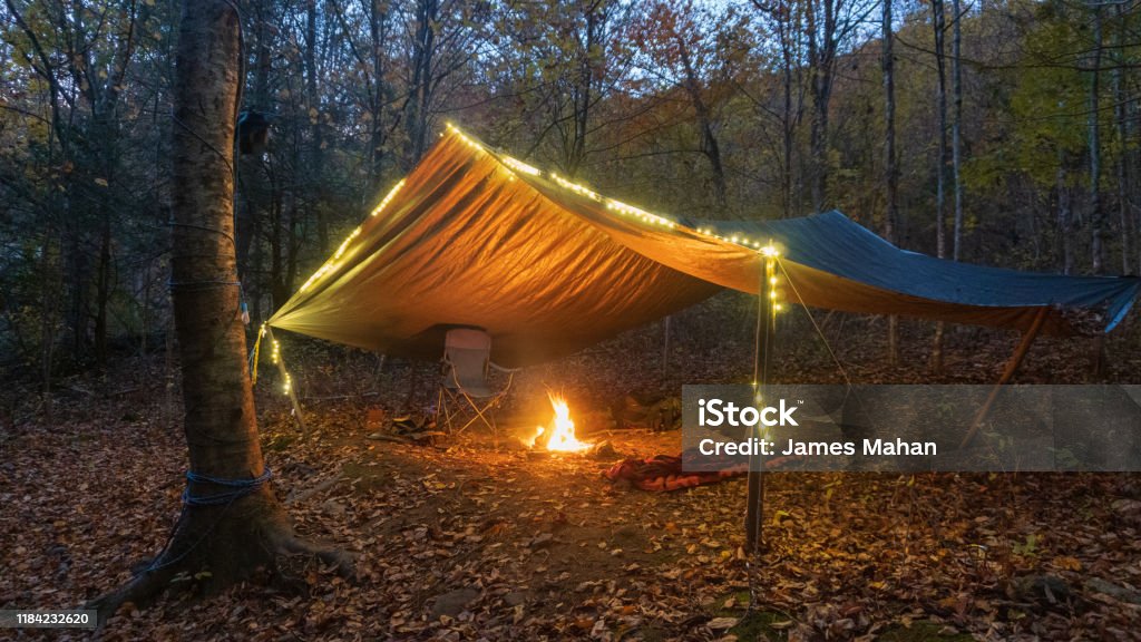Primitive Tarp Shelter with campfire and fairy lights. Survival Bushcraft setup in the Blue Ridge Mountains near Asheville. During autumn / fall season. Adventure Stock Photo