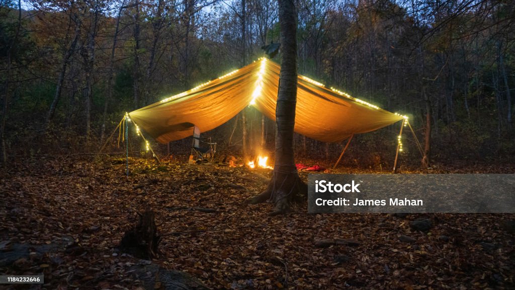 Primitive Tarp Shelter with campfire and fairy lights. Survival Bushcraft setup in the Blue Ridge Mountains near Asheville. During autumn / fall season. Camping Stock Photo