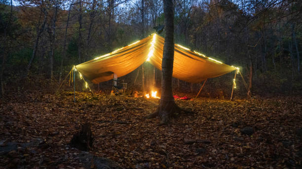 Primitive Tarp Shelter with campfire and fairy lights. Survival Bushcraft setup in the Blue Ridge Mountains near Asheville. During autumn / fall season. stock photo