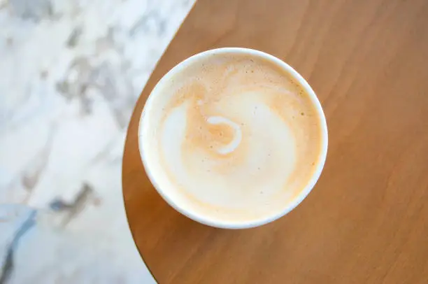 Fresh cappuccino in a paper cup on a wooden table in a cafe. Coffee to go.