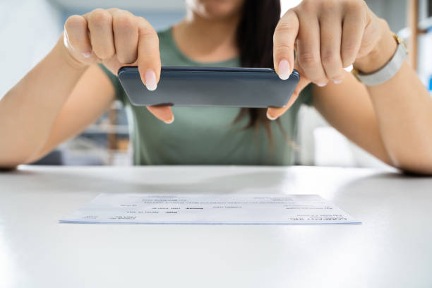 Woman Taking Photo Of Cheque To Make Remote Deposit Woman Taking Photo Of Cheque To Make Remote Deposit In Bank bank deposit slip photos stock pictures, royalty-free photos & images