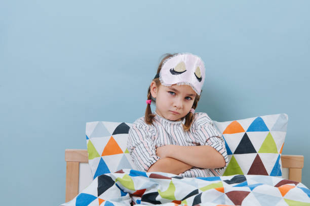 気分を害された小さな女の子は、手を組んでパジャマでベッドに座っています - anger child braids braided ストックフォトと画像