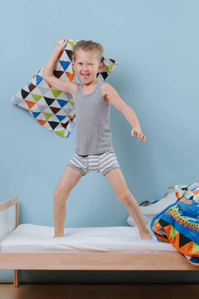 istock little boy standing on bed, ready for a pillow fight over blue walls 1184244871