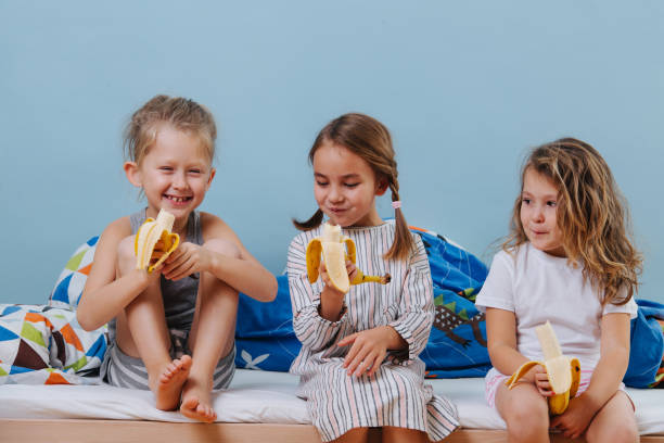 istock Three kids in sleeping clothes sitting on unmade bed, eating bananas 1184244885