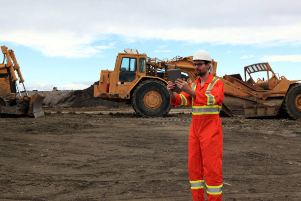 Male Construction worker looking at tablet at work site in front of heavy construction equipment at Cochrane, Alberta, Canada cochrane alberta photos stock pictures, royalty-free photos & images