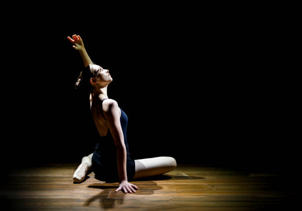 istock Young woman dancing ballet on stage against dark background 1184246191