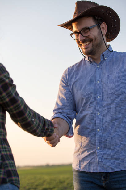 istock Two farmers shaking hands in field 1184246979