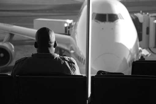 Johannesburg, Gauteng, South Africa - July 16, 2009: African passenger seated on lounge waiting for his flight, looking to airplane parked on Tambo International Airport runway