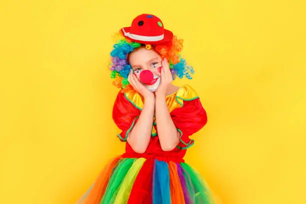 Photo of Funny little kid wearing clown costume touches cheeks and smiling