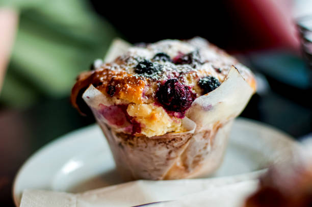 Stock photo showing elevated view of muffin baking tray containing homemade blueberry muffins in paper cake cases and fresh blueberries. Home baking concept.