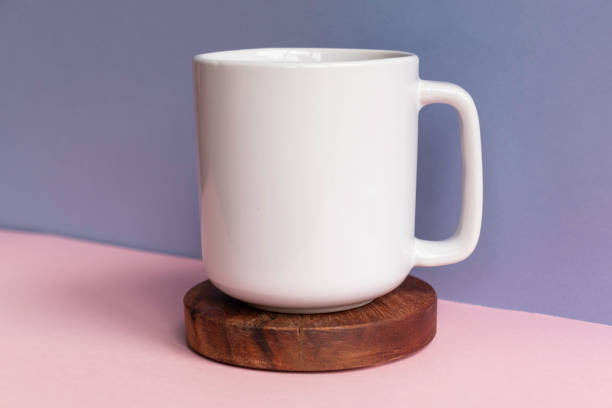 istock Blank white coffee mug on dark wooden coaster against a blue and pink background - plain cup mock up template for retail 1184278106